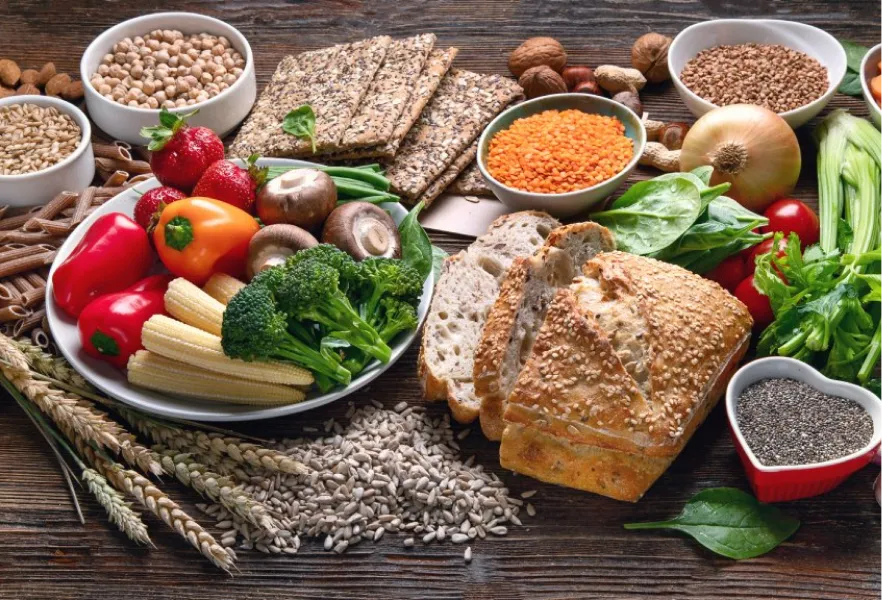 Variedad de alimentos ricos en fibra como verduras, cereales integrales, legumbres y semillas en una mesa de madera