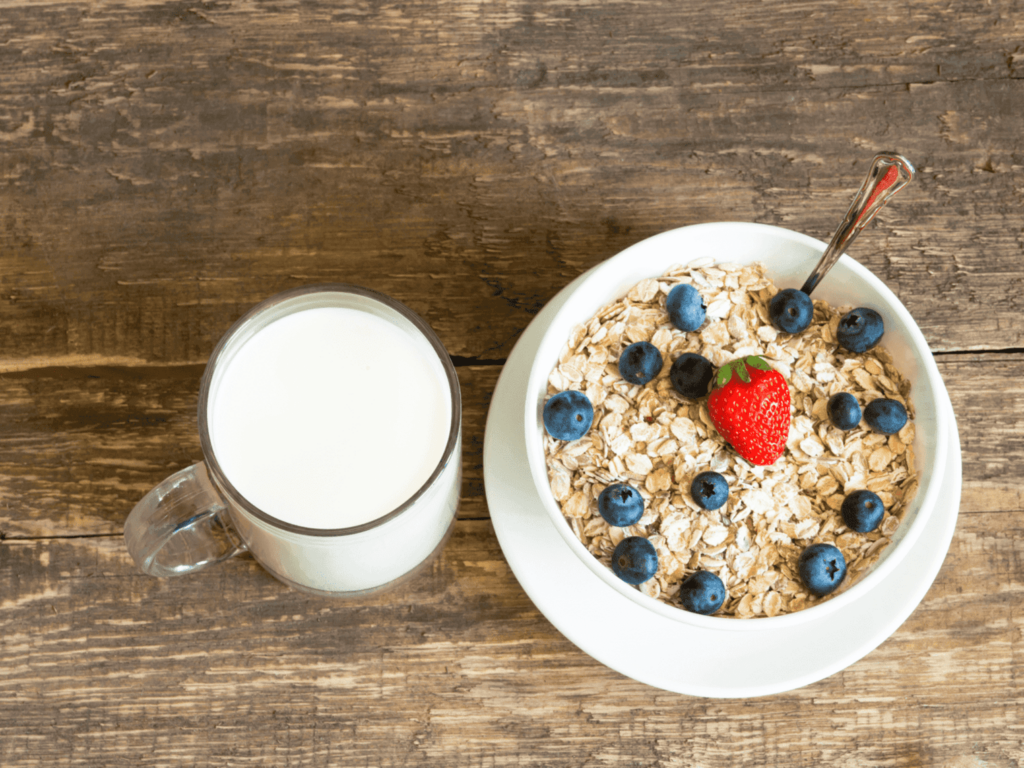 Desayuno dulce con una taza de leche y un tazón de avena, fresas y arándanos.