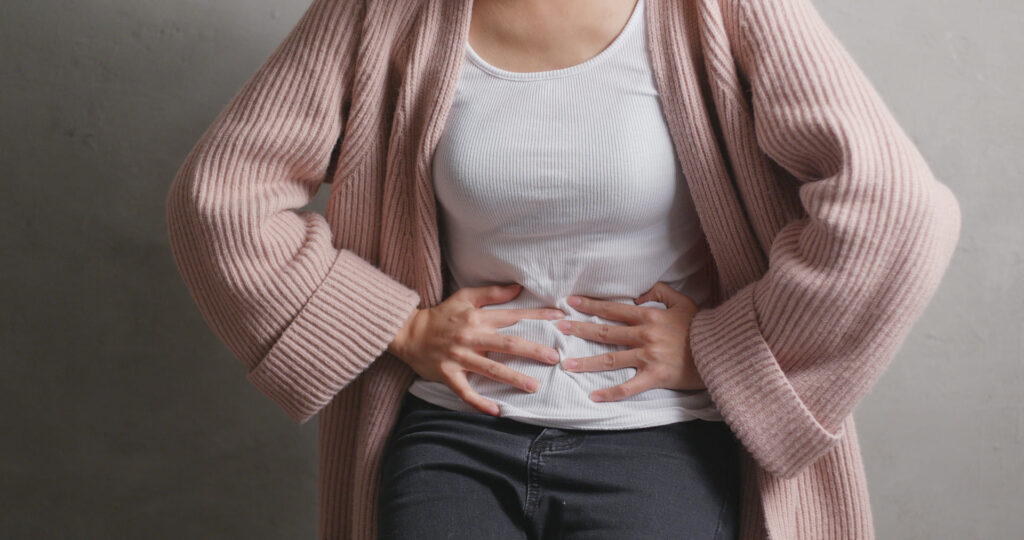 Mujer con suéter rosa presionando su abdomen con ambas manos debido a molestias digestivas