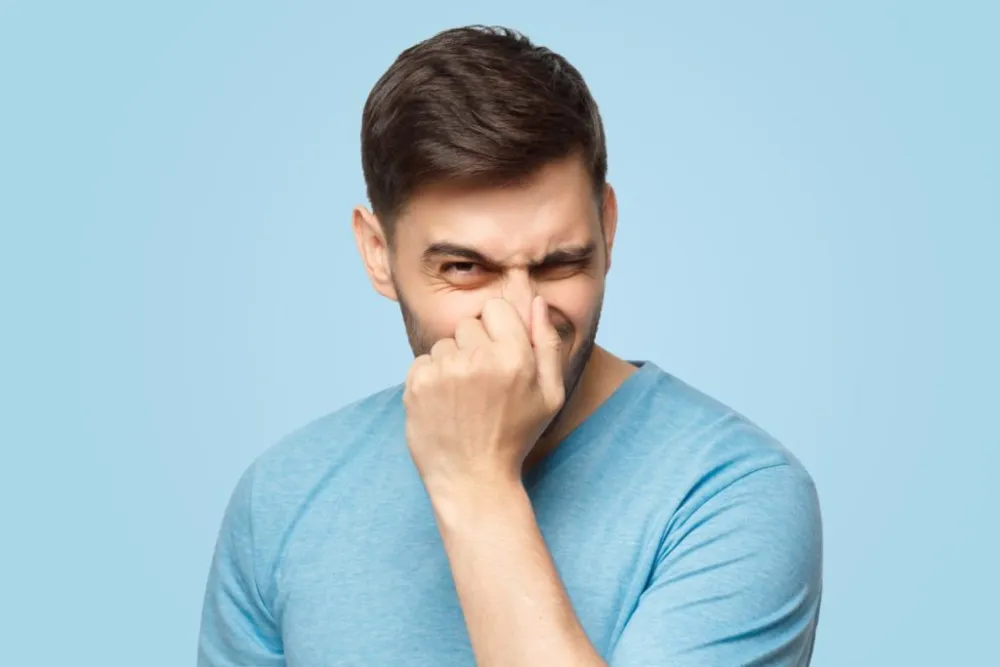 Hombre con camiseta azul se tapa la nariz con gesto de desagrado por mal olor