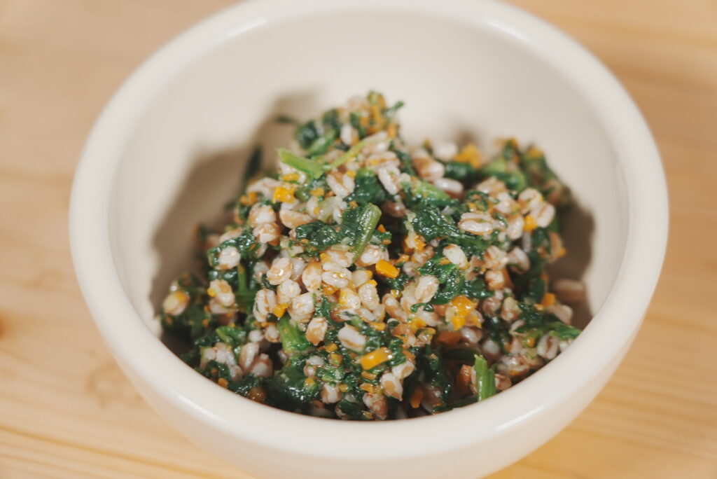 Bol de espelta mezclada con espinacas, zanahorias y verduras, servida en un pequeño recipiente blanco.