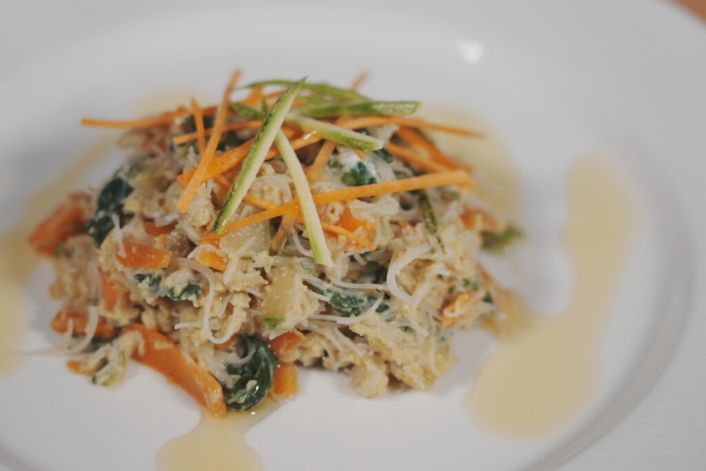 Plato de fideos de arroz con verduras y huevo, acompañado de tiras de zanahoria y calabacín.