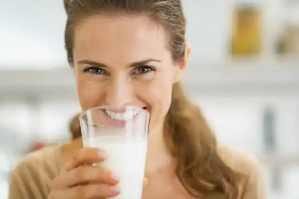 Mujer sonriente bebiendo un vaso de leche vegetal sin lactosa, opción apta para la salud intestinal